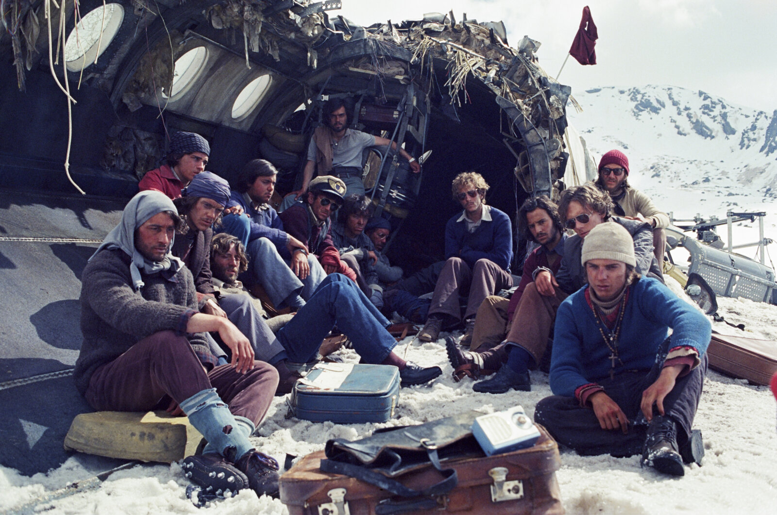 Eine Szene aus Die Schneegesellschaft: Die Überlebenden des Flugzeugabsturzes sitzen vor dem Wrack des Flugzeuges.