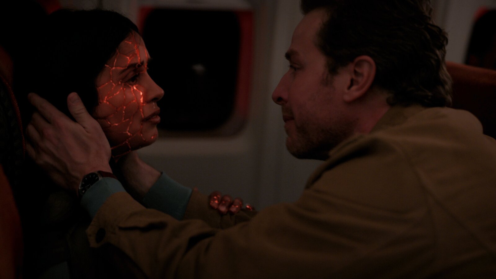 Eine Szene aus der finalen Episode "Final Boarding" von Manifest, Staffel 4: Saanvi hat rote Risse im Gesicht und ist kurz davor, zu sterben, doch Ben, der ihr Gesicht in den Händen hält, will das nicht zulassen.