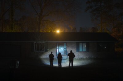 Drei Ermittler*innen aus der neuen Netflix-True-Crime-Serie "Missing: Dead or Alive?" leuchten mit ihren Taschenlampen ein leerstehendes Haus an.